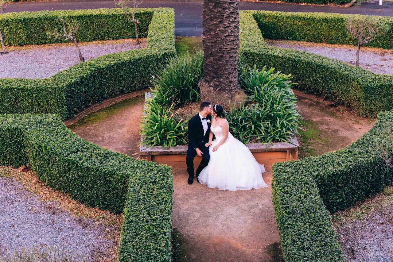 Bride and groom kiss in a picturesque garden setting, surrounded by lush greenery.